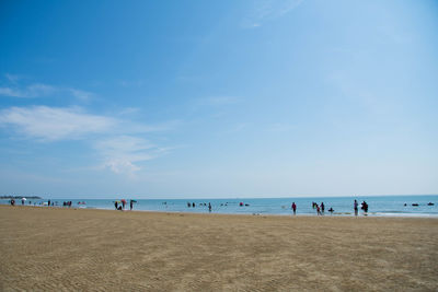 People on shore at beach against blue sky