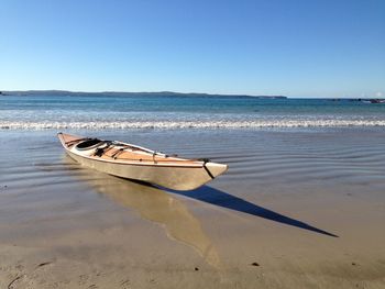 Boat moored on beach against clear sky