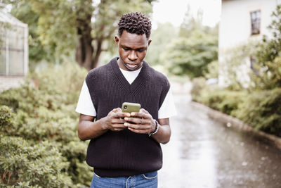 Young sad african man typing message, texting on phone in rain outdoor