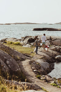 Rear view of teenage boy with sibling walking by father over rocky land during weekend