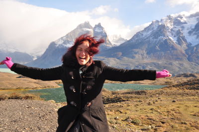 Portrait of smiling young woman standing on mountain against sky