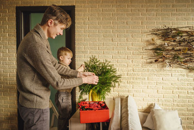 Father and son decorating the christmas tree against wall