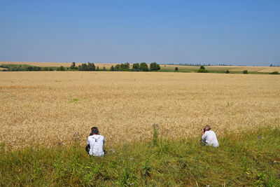 Rear view of people photographing while crouching by wheat field