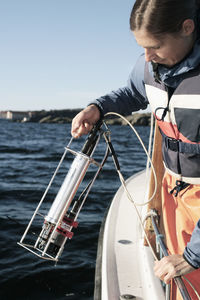 Woman holding water sampling equipment while standing in boat on river