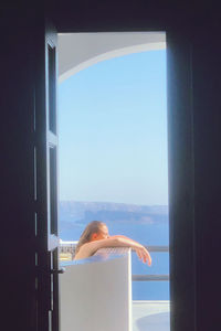 Rear view of woman looking at sea seen through window