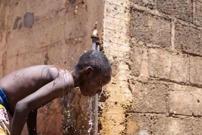 Boy bathing under faucet