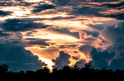 Low angle view of silhouette trees against dramatic sky