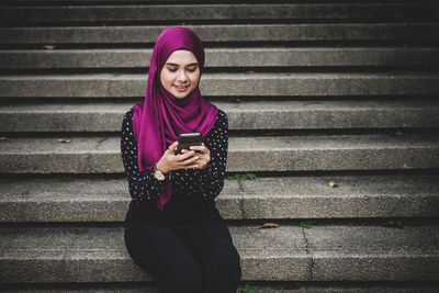 Smiling young woman using mobile phone on staircase