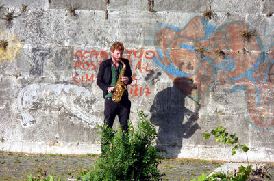 Young man playing saxophone against graffiti wall