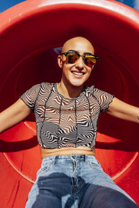 Happy woman with shaved head wearing sunglasses sitting in slide