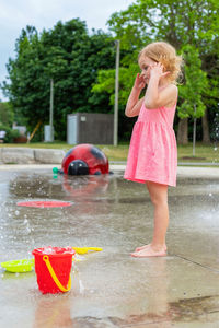 Small beautiful girl in pink dress having fun at splash pad fountain playground.