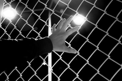 Close-up of hand touching chainlink fence at night