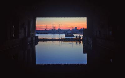 Silhouette buildings by lake against sky during sunset