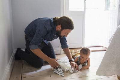 Mid adult father cleaning floor by baby boy at home