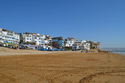 Buildings by sea against clear blue sky