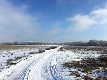 Snow covered road amidst field against sky