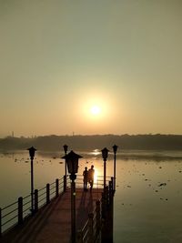 Silhouette people on lake against sky during sunset