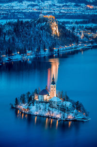 Illuminated building by lake at dusk