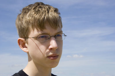 Close-up of thoughtful teenage boy wearing sunglasses while looking away against sky