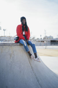 Full length portrait of young man sitting against sky