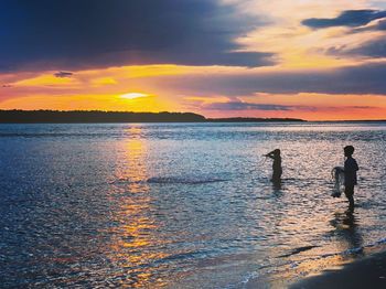 Silhouette people on beach against sky during sunset