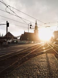 Railroad tracks by city against sky during sunset