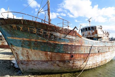 Abandoned boat moored at shore against sky