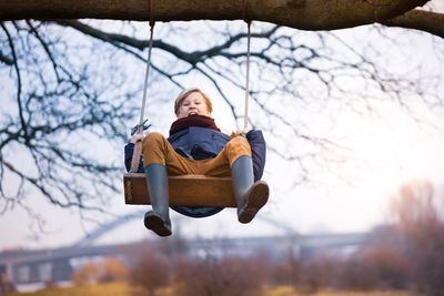 Full length portrait of boy swinging on rope swing