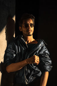 Portrait of young man standing against black background