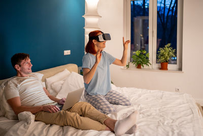 Side view of woman sitting on bed at home