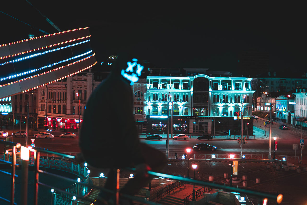 BLURRED MOTION OF MAN STANDING ON ILLUMINATED STREET AT NIGHT