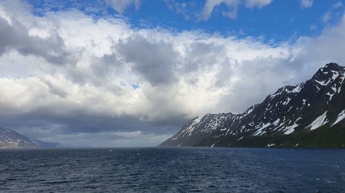 Scenic view of sea by snowcapped mountains against sky