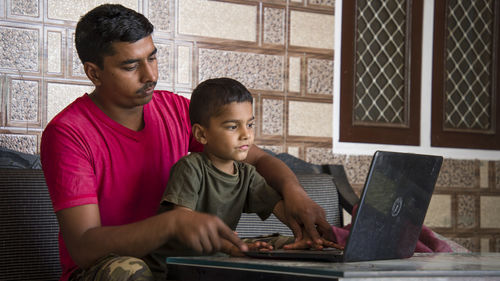 Indian father teaching adorable little son to use laptop. online study concept.