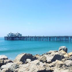 Pier on sea against clear blue sky