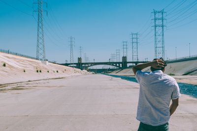 Rear view of man standing against bridge over canal