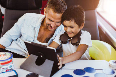 Smiling father and son using digital tablet while sitting in train