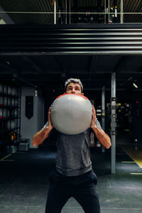 Strong determined athletic male holding medicine ball during workout in gym
