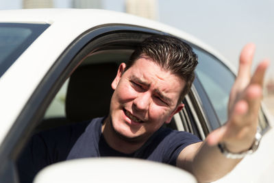 Frustrated man gesturing through window while traveling in car