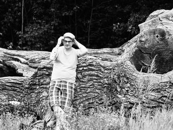 Full length portrait of smiling young woman standing on tree trunk in forest