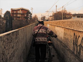 Rear view of man with bicycle on walkway in city