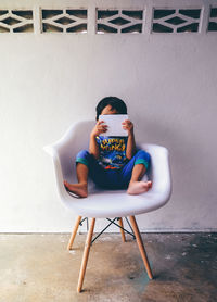 Boy sitting on chair against wall