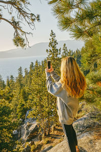 Young woman taking a picture of sunset over lake tahoe.