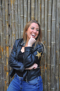 Portrait of smiling young woman standing against wooden fence