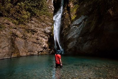 Rear view of man standing in lake against waterfall