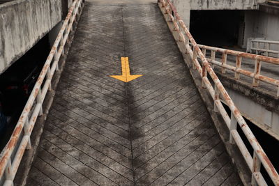 High angle view of arrow sign on footpath by building