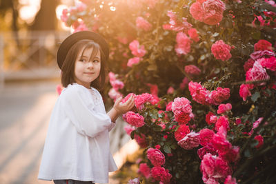 Cute stylish child girl 5-6 year old wear trendy clothes and hat posing over flower rose outdoors