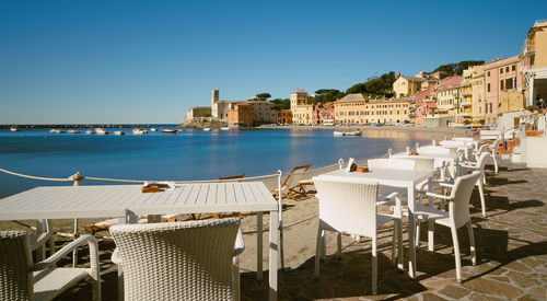 Empty table and chairs arranging by sea against sky