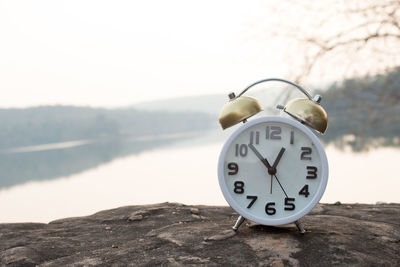 Alarm clock on cliff against lake