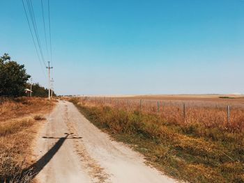 Dirt road amidst field against clear blue sky