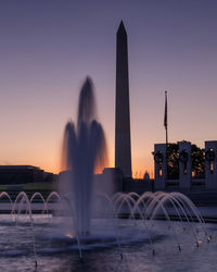 Fountain in city against sky during sunset